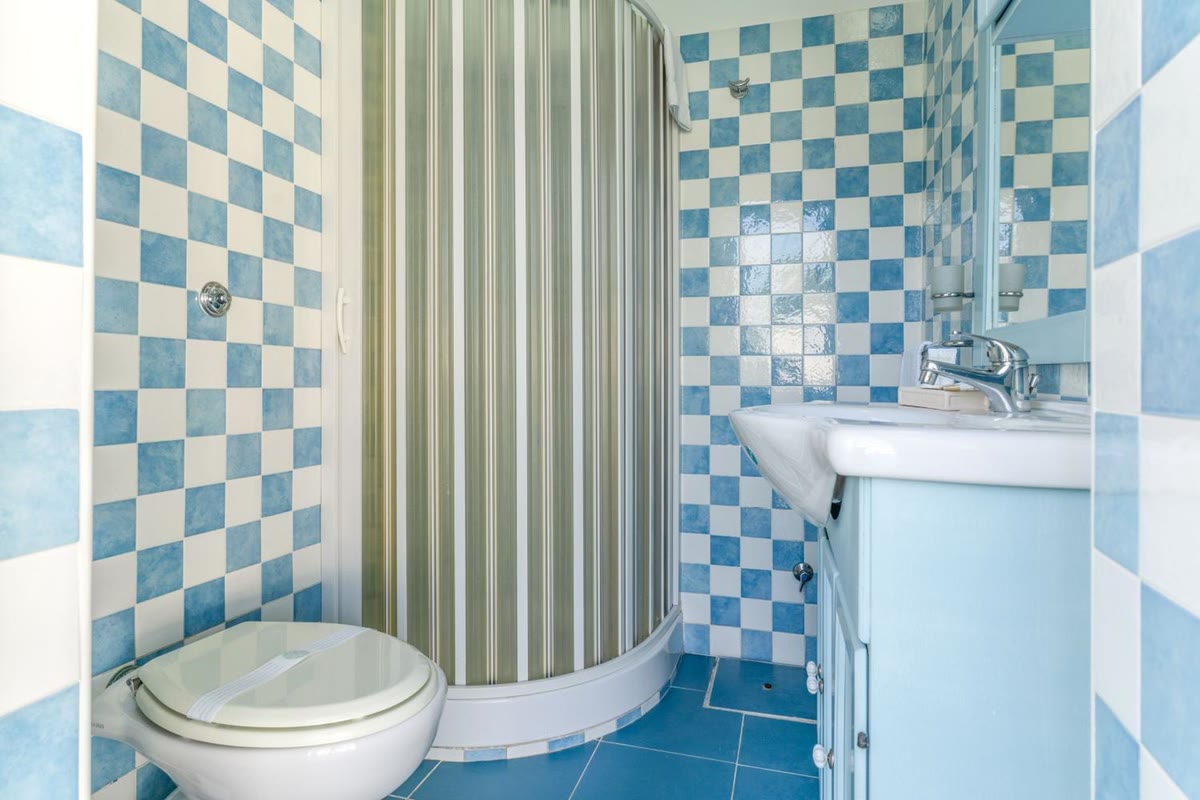 Il bagno a quadretti azzurri e bianchi, con la doccia ad angolo e il lavabo