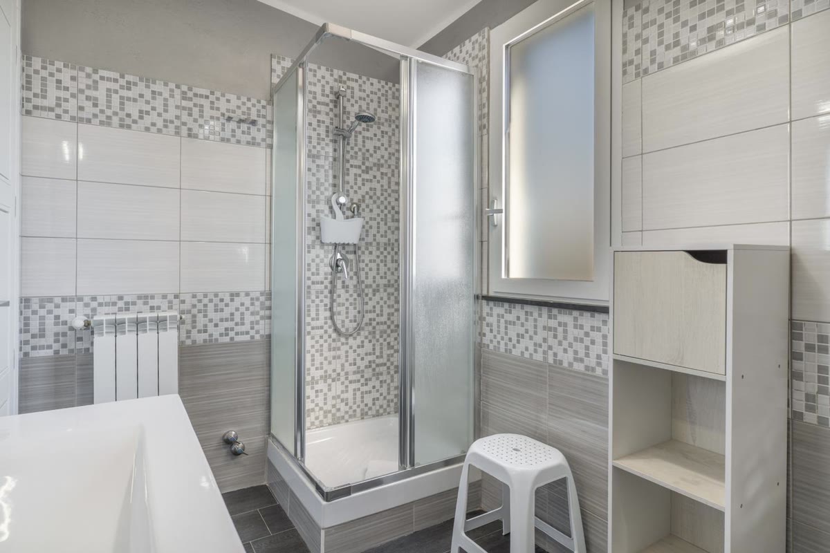 Il bagno con il box doccia, piastrelle bianche e mosaico grigio