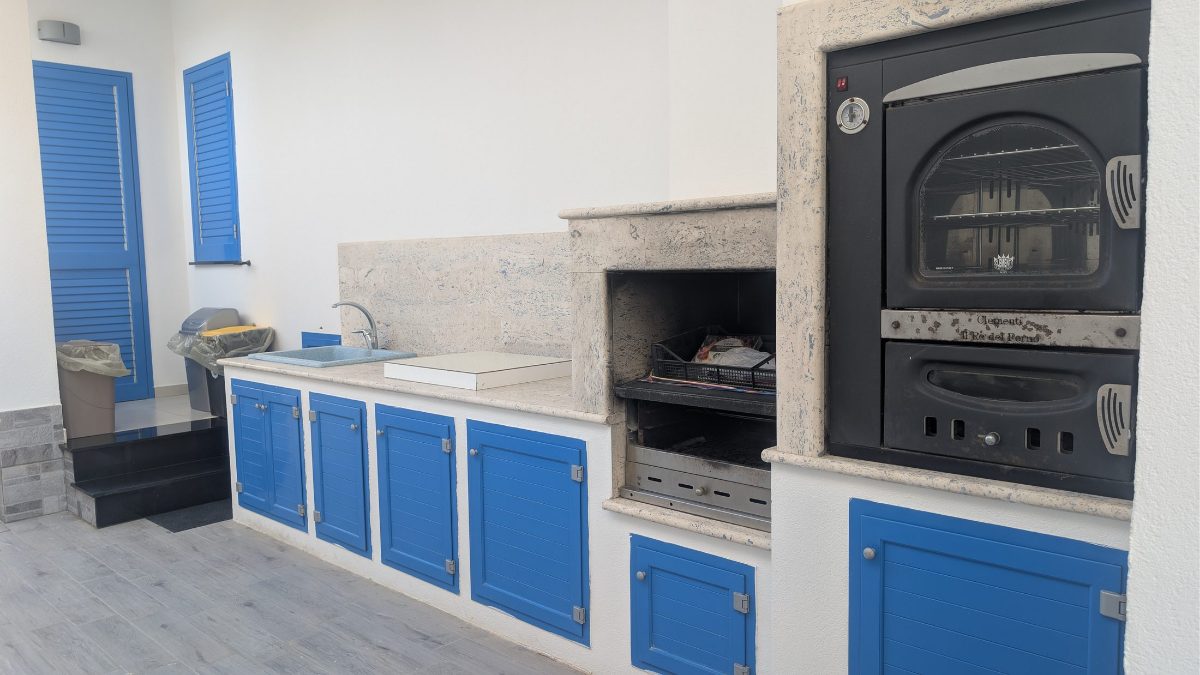 La cucina esterna da vicino: ante blu e forno a legna
