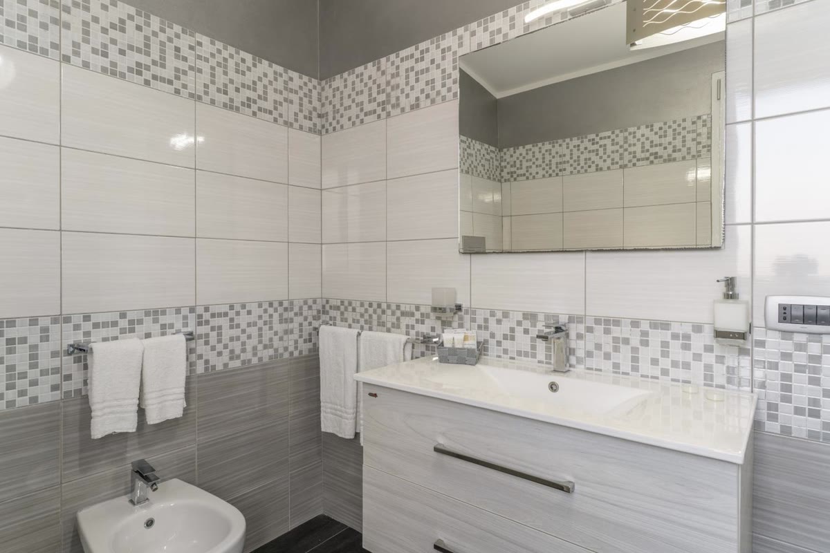 Bathroom with white tiles and grey mosaic: vanity unit, mirror and bidet