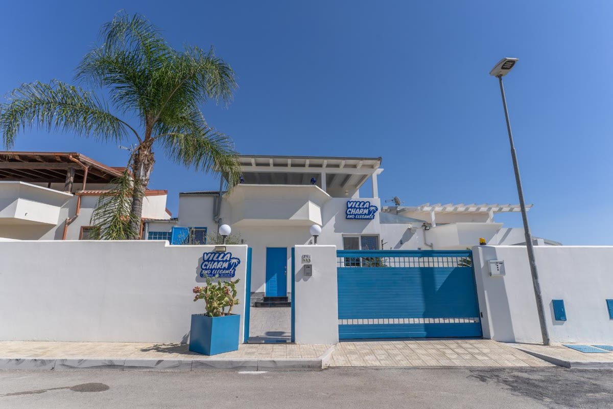 The villa seen from the road, with palm trees and the blue gate